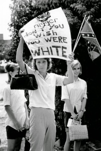 A woman stands on the side of the road challenging civil rights marchers with a hand written sign. Bogalusa, Louisiana, in 1965. Photograph by Matt Herron